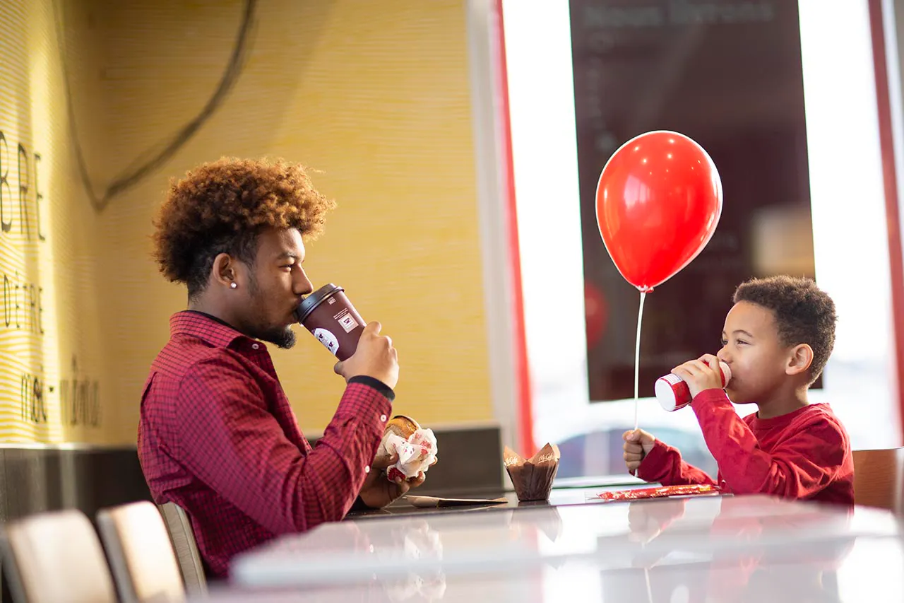 Un joven y un niño con un globo rojo merendando en un restaurante McDonald's