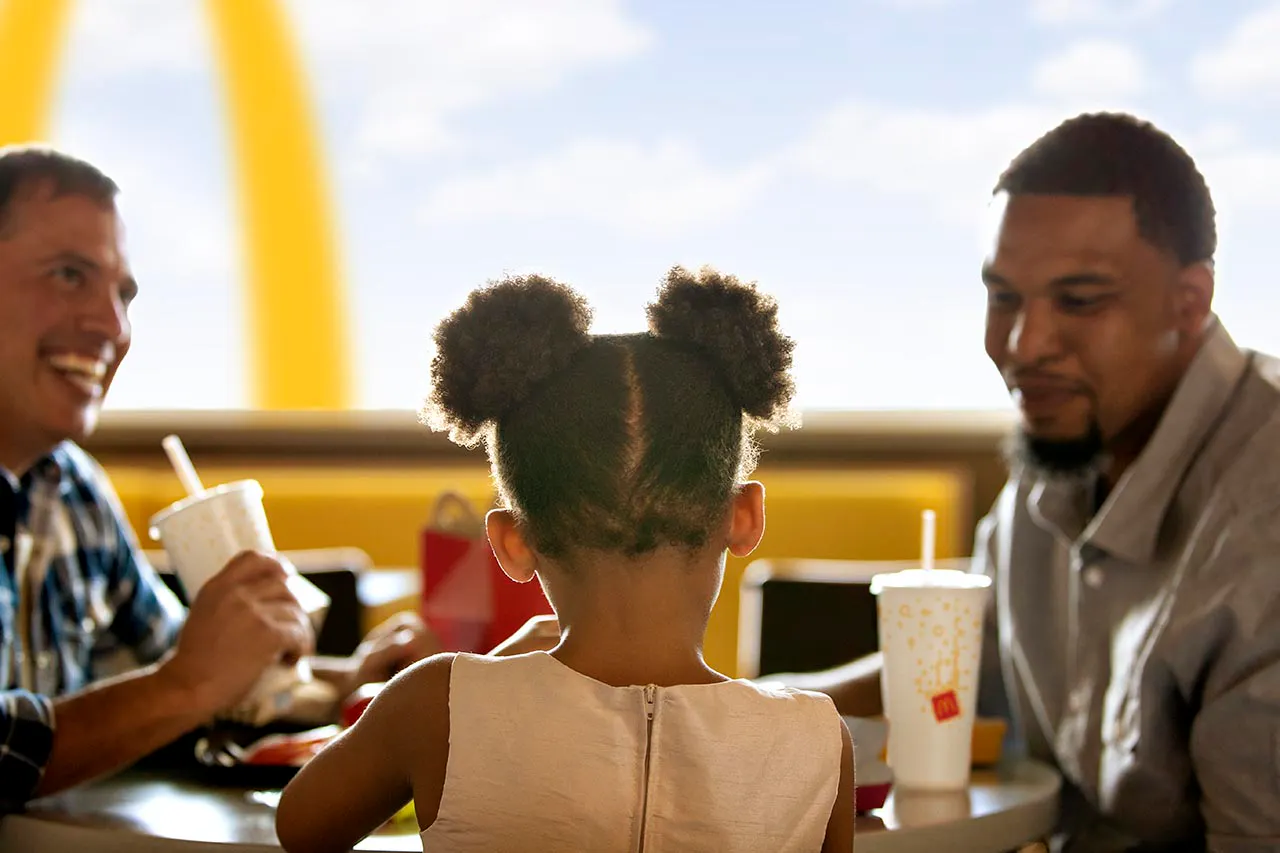 Una niña de espaldas comiendo con dos adultos en un restaurante McDonald's