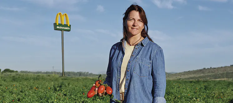 Dona al mig del camp amb braços plegats i un tractor vermell al fons