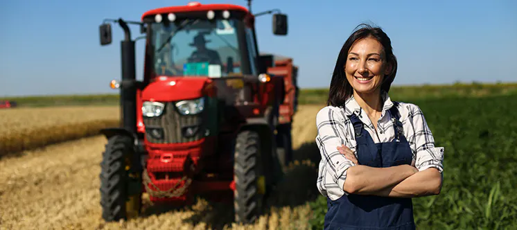 Mujer en medio del campo, con los brazos cruzados y un tractor rojo al fondo.