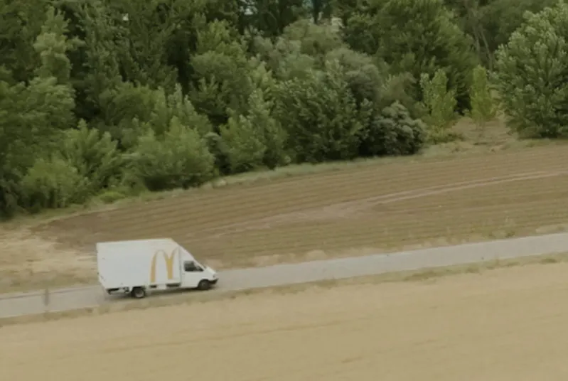 Camión con el logo de McDonalds en la parte trasera lateral circulando por una carretera con un bosque de fondo