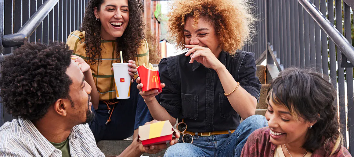 Grup d'amics asseguts a unes escales mentre comparteixen un menú de McDonalds